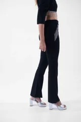 Pantalón negro de corte flare, tiro alto, con detalles de flecos de strass en los bolsillos laterales.