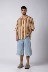 Camisa de manga corta confeccionada en tejido de crochet con diseño de ondas verticales en tonos tierra y beige. Presenta cuello solapa y cierre frontal con botones.