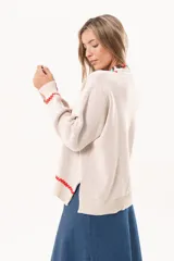 Sweater tejido color crudo con cuello redondo y mangas largas. Presenta dos peces rojos con detalles en azul bordados en el frente. Tiene ribete ondulado rojo en cuello, puños y ruedo.