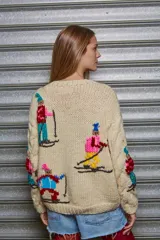 Sweater tejido de lana color beige con cuello redondo y mangas largas. Presenta bordados de figuras esquiando en distintos colores.