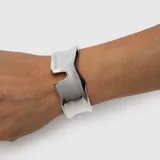 Brazalete ancho plateado de diseño rígido y líneas orgánicas, con acabado brillante y estilo moderno.