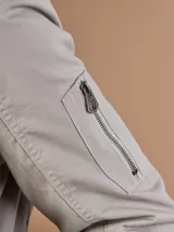 Campera bomber gris claro con cierre frontal y bolsillos laterales.