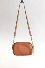 Cartera bandolera negra con diseño capitoneado en forma de V, correa de cuero y cadena plateada, cierre metálico y doble bolsillo interior.