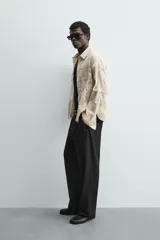 Camisa de corte relajado confeccionada en una mezcla de algodón y lino con textura semitransparente. Presenta un diseño de rayas verticales, cuello solapa, manga larga con puños abotonados y cierre frontal con botones.
