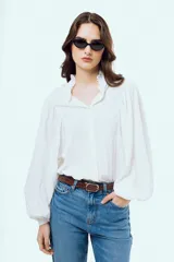 Camisa blanca de manga larga abullonada, con cuello alto y volados delicados en el borde.