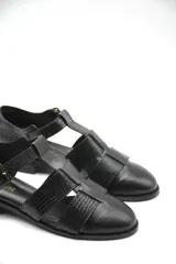 Zapato tipo cangrejera de cuero color marrón, con diseño de tiras entrelazadas, punta cerrada y pulsera con hebilla ajustable al tobillo. Cuenta con un taco bajo de madera.