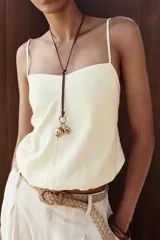 Top corto de lino color crema, con escote en pico y tirantes finos. Presenta un diseño abullonado en el bajo con elástico interior y espalda abierta con tira elástica horizontal.
