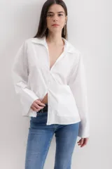Camisa blanca de algodón, de corte holgado, con cuello clásico, mangas largas con puños anchos y un bolsillo de parche en el lateral.