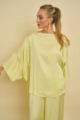 Blusa de satén de seda color verde claro, con cuello bote y mangas amplias tipo murciélago de corte holgado.