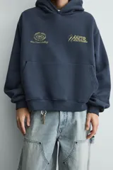 Sudadera tipo hoodie de corte relajado en color azul oscuro con efecto lavado. Presenta capucha, manga larga, bolsillo frontal tipo canguro y detalles estampados en color dorado en el pecho.