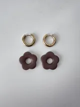 Aros de acero quirúrgico dorados con argollas pequeñas y dijes colgantes en forma de flor color celeste.
