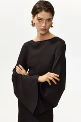 Vestido midi negro con textura, escote bote, mangas largas tipo trompeta y diseño ajustado con frunces laterales que generan un efecto drapeado.