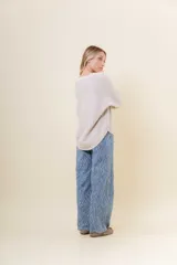 Buzo tejido de punto en color beige, con cuello redondo, mangas largas y silueta relajada con dobladillo irregular, siendo más largo en la parte trasera.