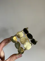 Brazalete rígido de bronce dorado con apliques circulares.