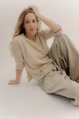 Buzo básico color beige confeccionado en lambswool, con escote en V, mangas 3/4 y tajos laterales. Presenta un logo bordado en el bajo.