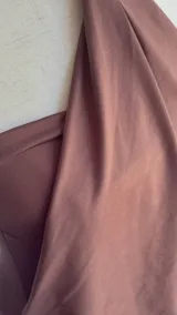 Vestido corto marrón oscuro, estilo halter con cuello anudado en una argolla central. Presenta un diseño drapeado en la parte superior que cae sobre una falda ajustada.