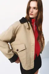 Campera levemente acolchada en lona de algodón gruesa color beige, con cuello y puños vueltos de efecto cuero marrón oscuro. Presenta cierre frontal con botones, solapa rompevientos, bolsillos delanteros de parche con solapa y bolsillos calientamanos.