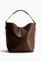 Cartera shopper de diseño slouchy en color marrón, con correa ajustable en la parte superior y detalles de tiras colgantes en los laterales con hebillas metálicas.