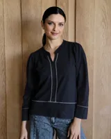 Remera de algodón color negro con cuello mao y escote en V. Presenta costuras decorativas en color blanco a lo largo del frente, en el ruedo y en los puños. Tiene mangas largas con un ligero fruncido en los hombros.