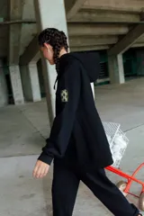 Buzo negro oversize de frisa con capucha amplia, bolsillo canguro, terminaciones de puño y ruedo con rib, y logo bordado en el centro delantero.