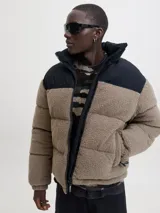 Campera puffer con diseño de bloques de color, combinando tejido teddy en tono arena y paneles negros en los hombros. Presenta cuello alto, cierre frontal y diseño acolchado.