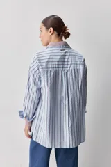 Camisa de calce relajado con diseño a rayas verticales en tonos azul y blanco, cuello clásico, mangas largas con puños abotonados y cierre frontal con botones. Presenta bolsillos aplicados en el delantero y una silueta versátil.