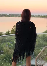 Ruana tejida artesanalmente en lana merino, de color negro, con diseño calado y terminación de flecos largos en los bordes.