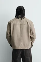 Sobrecamisa boxy fit de hombre confeccionada en tejido efecto ante color beige, con cuello solapa, manga larga con puño abotonado, bolsillo de parche en el pecho y cierre frontal con botones a presión ocultos.