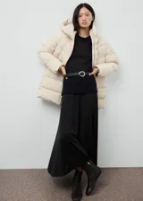 Campera acolchada de corte recto y diseño puffer, color beige, con capucha, cuello alto y cierre frontal de cremallera doble. Cuenta con mangas largas con puños elásticos y dos bolsillos laterales con cierre.