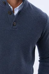 Buzo tejido texturado color verde oscuro, con cuello alto y cierre parcial de tres botones. Tiene mangas largas y un pequeño detalle de etiqueta marrón en el dobladillo inferior.