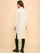 Cardigan largo de tejido color beige claro, sin cuello, con bolsillos frontales y detalles de pespuntes decorativos a lo largo del borde frontal.