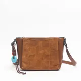 Bandolera de tamaño mediano en color marrón, confeccionada con una combinación de cuero sintético liso en los laterales y gamuza con costuras decorativas en el panel frontal. Incluye una correa ajustable y un colgante decorativo con cuentas de colores y cordón trenzado.