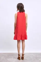 Vestido corto blanco sin mangas, con escote en V y detalle de broche dorado en el centro. La falda tiene un volado en el ruedo.