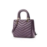 Cartera de mano color púrpura, con diseño acolchado en símil cuero soft y costuras a tono. Tiene acceso con cierre y broches imantados, herrajes dorados y correa regulable para usar como bandolera. El interior está forrado en tela de algodón y poliéster, con un bolsillo con cierre y dos abiertos.