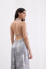 Vestido largo de fiesta color plateado con acabado metalizado, escote halter con detalle de nudo y espalda descubierta.
