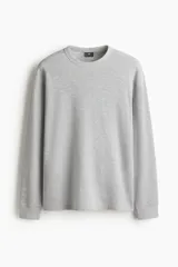 Conjunto de pijama de dos piezas en punto waffle gris claro, compuesto por una remera de manga larga con cuello redondo y un pantalón con cintura elástica y cordón de ajuste.