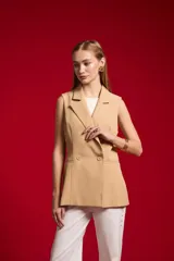 Chaleco sastrero de poliéster color beige, con solapa ancha, doble botonadura frontal y bolsillos de ribete simulados.