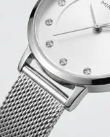 Reloj analógico de mujer con caja redonda plateada, esfera minimalista con índices de puntos y malla de acero tipo milanesa. Diseño elegante y versátil.