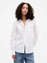 Camisa blanca de manga larga con cuello camisero, cierre frontal de botones y un bolsillo en el pecho con un pequeño detalle bordado.