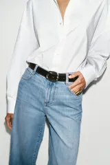 Jeans de tiro alto con pernera ancha y corte cropped. Presenta diseño de cinco bolsillos, cierre frontal con cremallera y botón, e incluye un cinturón oscuro con hebilla metálica.