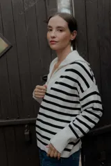 Buzo de punto con diseño a rayas horizontales en blanco y negro. Presenta cuello alto con cierre frontal parcial y mangas largas con puños acanalados.