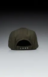 Gorra de estilo 5 paneles, color verde militar, con corona acolchada y visera negra. Presenta un pequeño parche negro con un logo blanco en forma de tijeras cruzadas.