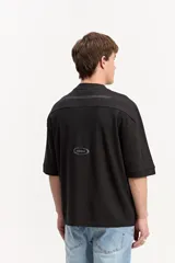 Remera negra de corte oversize, con mangas cortas amplias y cuello redondo ribeteado. Cuenta con una estampa frontal con la leyenda "Shift Mode" en tonos grises y texto secundario.