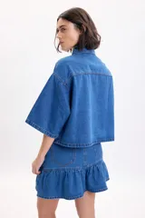 Sobrecamisa de jean de manga corta y corte oversize en color azul medio, con bolsillos frontales con solapa y cierre de botones metálicos a presión.