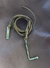 Collar de tiento de cuero marrón con dije de letra en bronce de textura irregular.