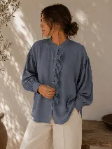 Camisa negra de calce relajado con cuello mao, cierre frontal de botones y detalle de volado vertical en el frente. Presenta mangas largas con puños abotonados.