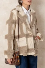 Chaqueta oversize con diseño de cuadros en relieve, confeccionada en una combinación de lana y poliéster con textura tipo borreguillo. Presenta un corte holgado, cuello con solapas y un botón joya central.