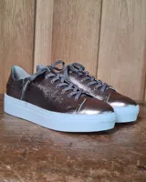 Zapatilla urbana de cuero con diseño combinado en color dorado metalizado y gamuza en tono tostado. Presenta cordones al tono, suela de goma blanca y detalles en cuero marrón en la parte posterior.