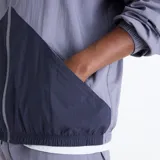Campera deportiva New Balance Sport Legacy en tonos gris y azul marino, con diseño de bloques de color, cuello alto, cierre frontal completo y el logotipo Flying NB bordado en el pecho.