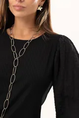 Blusa negra de tejido acanalado con mangas largas abullonadas de textura arrugada y puños elásticos.